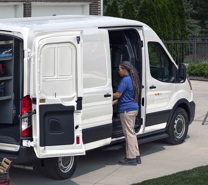 Rear view of a 2023 Transit® Cargo van parked in a driveway with the side and rear cargo doors open
