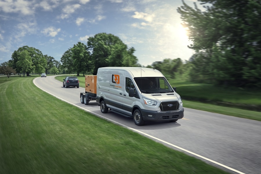 A 2023 Ford Transit® van being driven down a road towing a trailer