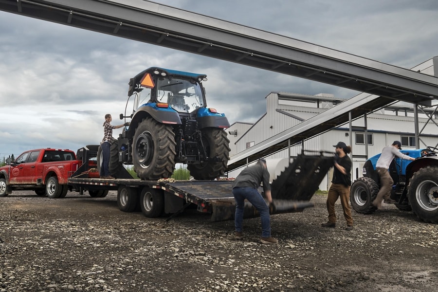 Men loading a tractor onto a trailer hitched to a 2023 Ford Super Duty® F-450® XL SuperCrew® Cab near a grain factory