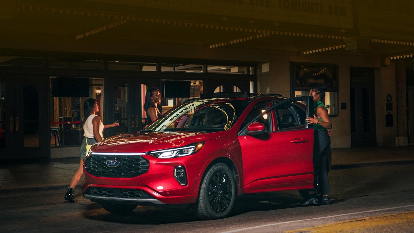 A 2023 Ford Escape® at night parked in front of a theatre woman getting in